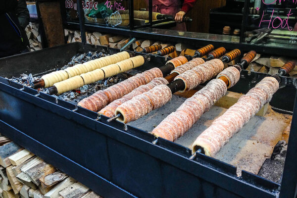 Trdelnik, traditional dessert baked in an open fire wooden stake in Prague Christmas Market, made from rolled dough that is wrapped around a stick, then grilled and topped with sugar and walnut mix