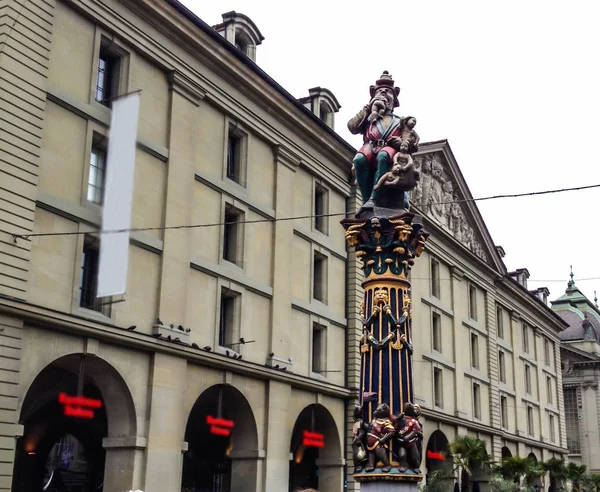 Hermosa vista de la calle de la ciudad de la estatua medieval colorida del ogro o del niño comedor en la parte superior de la fuente elaborada en Berna, Suiza. La fuente se atribuye a Hans Gieng en el siglo XVI . — Foto de Stock