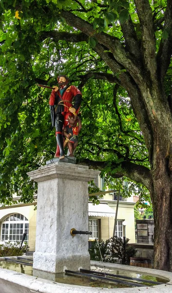 Hermosa vista de la calle de la ciudad de la estatua medieval colorida del mensajero en la parte superior de la fuente elaborada en Berna, Suiza. La fuente se atribuye a Hans Gieng en el siglo XVI . — Foto de Stock