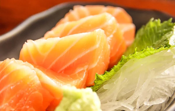 Японська кухня: лосось сашимі (свіжий лосось сировини) прикрашені тертий ріпи і м'яти leaf на дерев'яні таблиці як фон. — стокове фото