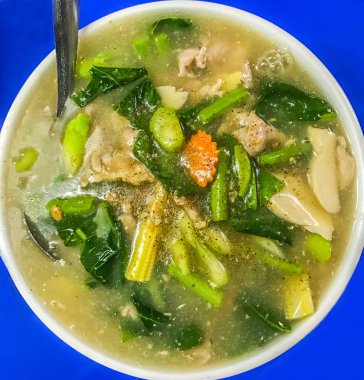 Düz geniş Fried noodle ile domuz eti ve kale, krem sos sos (Tay dili: Guaitiao Rad Na) mavi masa arka plan üzerinde beyaz kase. Popüler Asyalı Çinli Tay gıda cadde veya restoranlar bulundu.