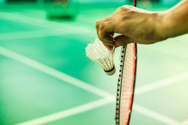 Closeup Badminton player hand holding the shuttle cock together with the racket, ready to serve position on the play green court with copy space