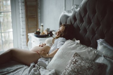 Kar-beyaz bir yatak odasında hamile bir kızla yatakta kahvaltı