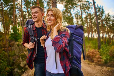 Sırt çantalı genç bir adam ve bir kadın orman yolu boyunca dağlarda yürüyüşe çıkıyorlar. Ormanda iki turistle yol. 
