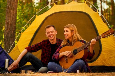 Ormanda kamp yapan çiftler. Mutlu ve rahatla. Genç adam ve kadın çadırın yanında oturuyor. Sırt çantasıyla gitar çalıyor, kahkahalarla gülüyor..