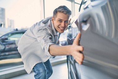 Stylish man rejoicing buying a new car in showroom. Buying and s