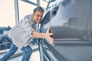 Stylish man rejoicing buying a new car in showroom. Buying and s
