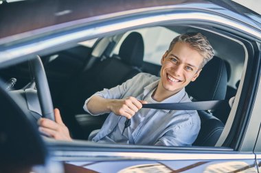 Caucasian man sitting in a new car hold a safety belt. 