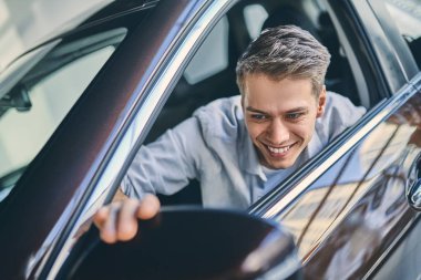 Happy buyer adjusting rear view mirrors in new car.