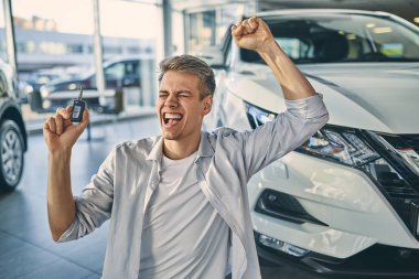 Happy man stand on knees rejoicing buying a new car in showroom.