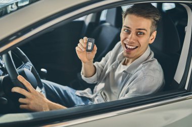 Smiling man holding a car key and sitting in new car. Business c