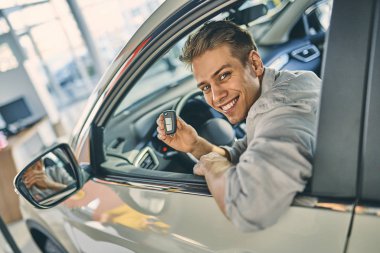 Smiling man holding a car key and sitting in new car. Business c
