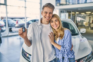 Happy girl and smiling man hold a key and standing behind a car.