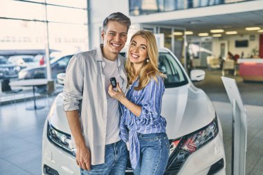 Happy girl and smiling man hold a key and standing behind a car.