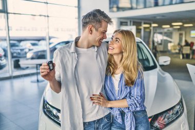 Happy girl and smiling man hold a key and standing behind a car.
