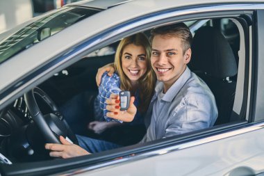 Happy couple holding a car key after buying it in showroom.
