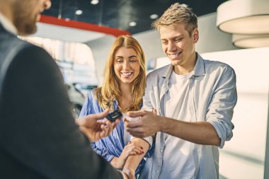 Happy couple getting a car key from stylish sale manager. 