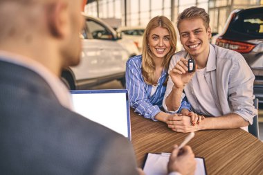 Happy cheerful girl getting a car key with handsome man in showr