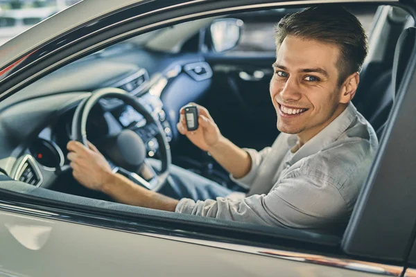 Smiling man holding a car key and sitting in new car. Business c