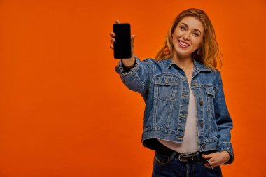 Kendine güvenen bir kadın telefon ekranı gösterir.