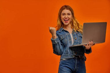 Kadın elinde dizüstü bilgisayarla muzaffer bir şekilde duruyor..