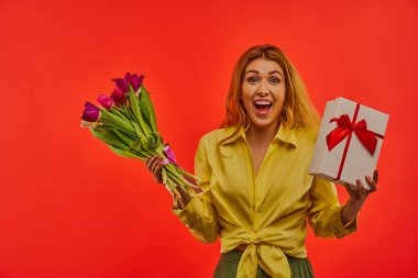 Bir buket çiçekli ve hediye kutusuyla mutlu bir bayan..