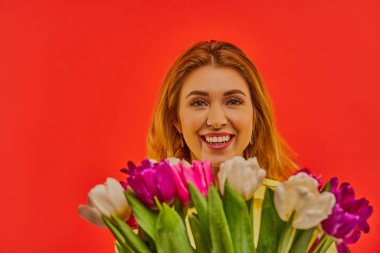 Bir buket lale ile kameraya gülümseyen bir kadın..