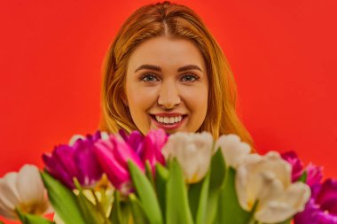 Bir buket lale ile kameraya gülümseyen bir kadın..