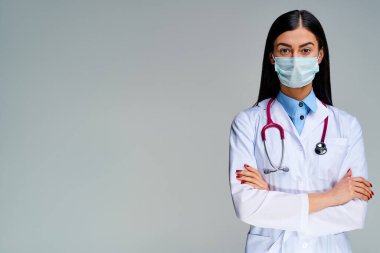 Kahverengi saçlı, doktor önlüklü, elleri katlı, kırmızı tırnaklı bir kadın.