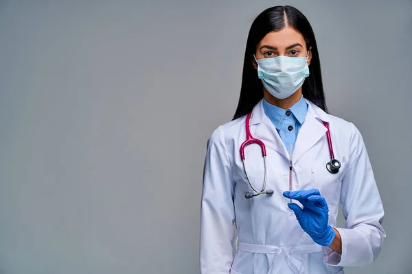 Woman in face mask with black hair in a medical coat with a syringe