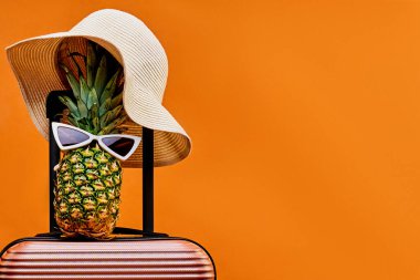 Tekerlekli bavulda güneş gözlüklü şapka ve ananas.