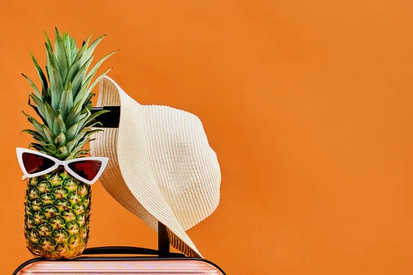 Tekerlekli bavulda güneş gözlüklü şapka ve ananas.