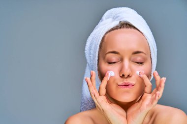 Saçında beyaz bir havlu ve yanaklarında krem olan mutlu kadını kapat.