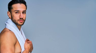 Beyaz banyo havlusu olan yakışıklı bir adam kameraya bakıyor.