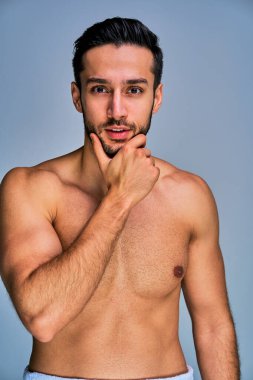 Mutlu, bronz tenli, siyah sakallı adam elleriyle yüzüne dokunuyor.