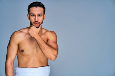 Siyah sakallı, beyaz banyo havlusuyla yüzüne dokunan kendinden emin bir adam.