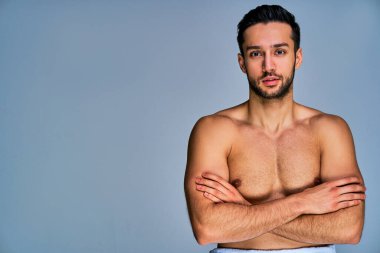 Siyah sakallı, beyaz bir havluyla kollarını kavuşturmuş kendinden emin bir adam.