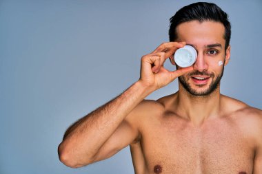 Siyah saçlı mutlu adam krema kavanozuyla gözlerini kapatıyor.