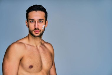 Siyah saçlı, yüzünde krem lekeleri olan, kameraya poz veren ciddi bir adam.