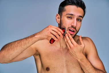 Suratı asık, yanağını elektrikli tıraş makinesiyle tıraş eden adam.