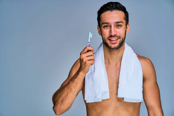 Happy tanned naked man with white bath towel on the neck with toothbrush