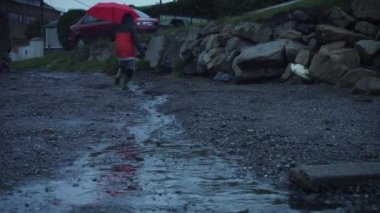 4 k çocuk şemsiye ile su birikintileri yağmurlu bir günde atlama
