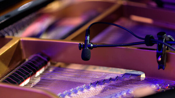 A microphone picks up the sweet melodies of a grand piano on a performance stage