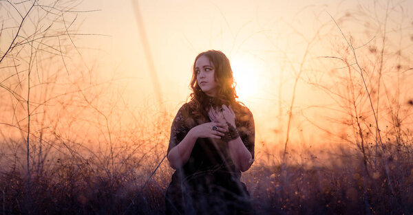 Fashion and editorial inspired. Brunette Model wearing lace dress and jewelry. Winged Eyeliner makeup. Shot in a dry brush field during golden hour