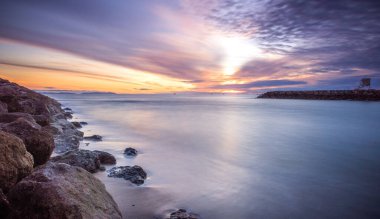 Kayalık bir iskelede bulutlu bir gün batımı