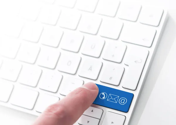 Dito premendo un tasto blu con simboli di comunicazione su un concetto di tastiera del computer — Foto Stock