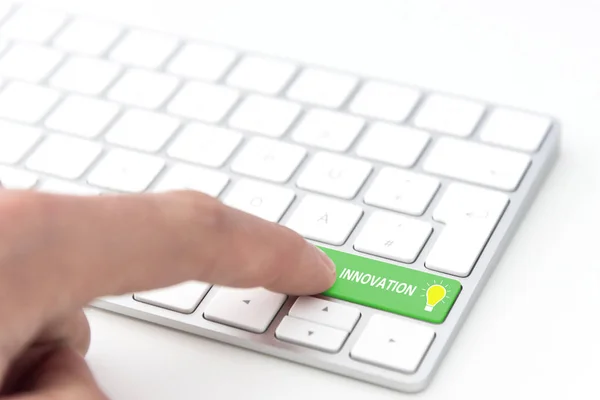 finger pressing a green key labeled INNOVATION with glowing light bulb symbol on a computer keyboard