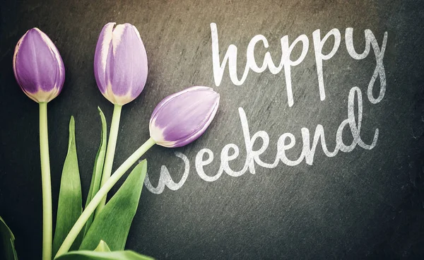 happy weekend greeting card top view of pastel purple tulips on dark gray slate blackboard background