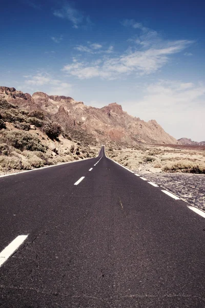 Largo camino recto a través del paisaje del desierto con montañas en el fondo bajo el cielo azul —  Fotos de Stock