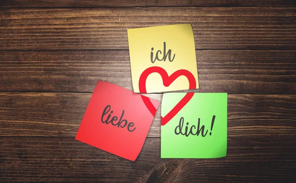 Notes collantes disant ich liebe dich (Je t'aime en allemand) et forme de coeur rouge sur planche de bois rustique fond de bois brun foncé — Photo